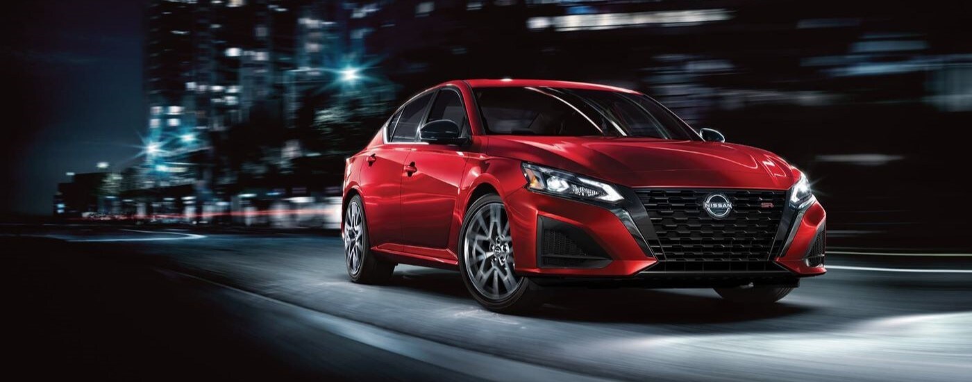 A red 2023 Nissan Altima SR is shown driving on a city street visiting used car dealers.